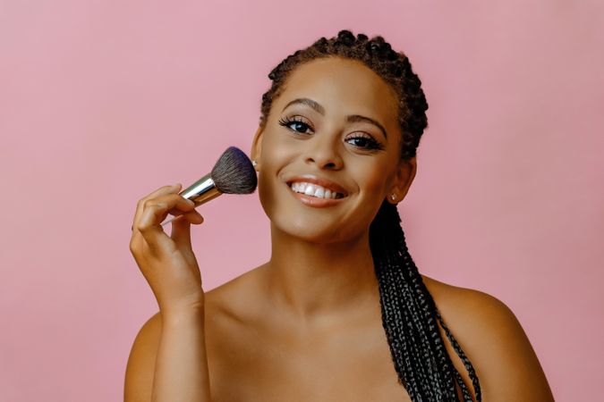 Happy Black woman with make up brush to her cheek