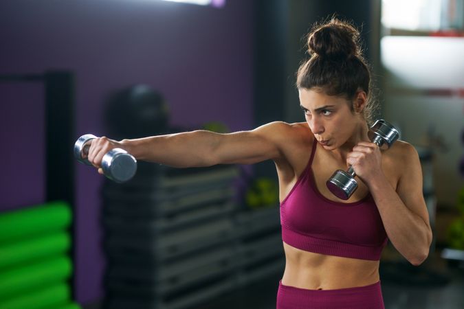 Healthy woman in gym holding small dumbbell in front of her