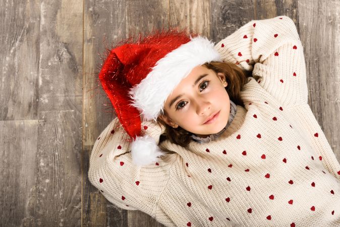 Girl in Santa hat lying on wooden floor