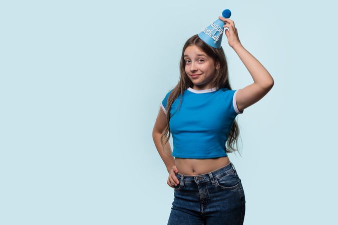 Girl adjusting birthday hat, showing playful and confident expression.