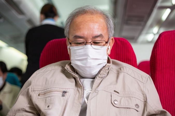 Portrait of older male wearing facemark and earbuds in flight