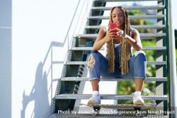 Female skater checking phone on stairs, copy space 5wE9mb