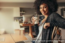Portrait of attractive woman with curly hair having coffee at home with a laptop. 4jQgr5