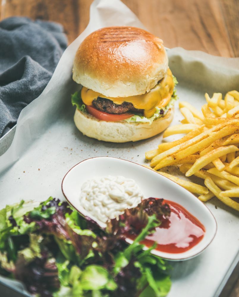 Top view of classic hamburger with fries and cottage cheese at wooden restaurant table