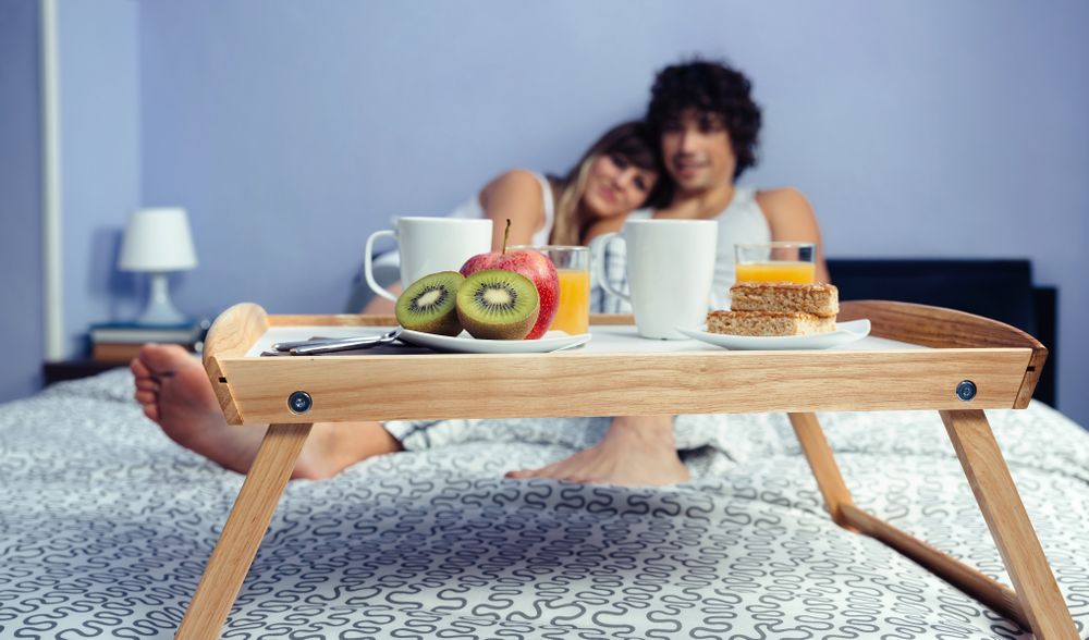 Healthy breakfast on tray and couple lying in background