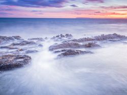 Sea waving near rough rocks during sunset