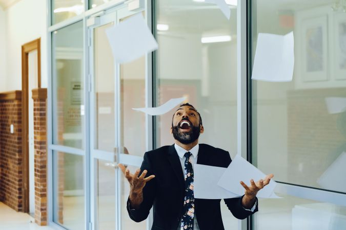Businessman in suit and tie celebrating by throwing papers in the air in office