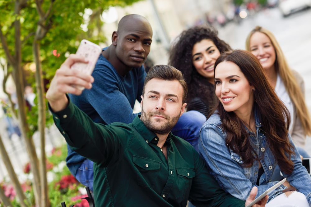 Group of friends taking selfie on phone on ledge outside