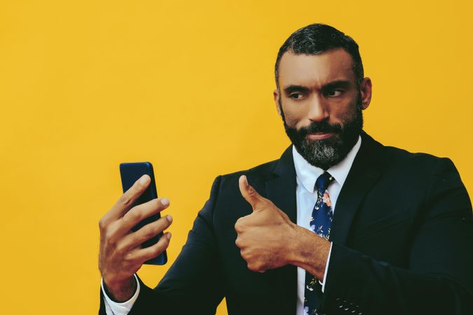 Serious Black businessman in suit giving thumbs up at smartphone screen