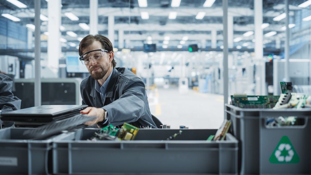 Male Worker Disassembling Old Laptops To Recycle Electronic Components For Sustainable Microchip Production At an Electronics Factory.