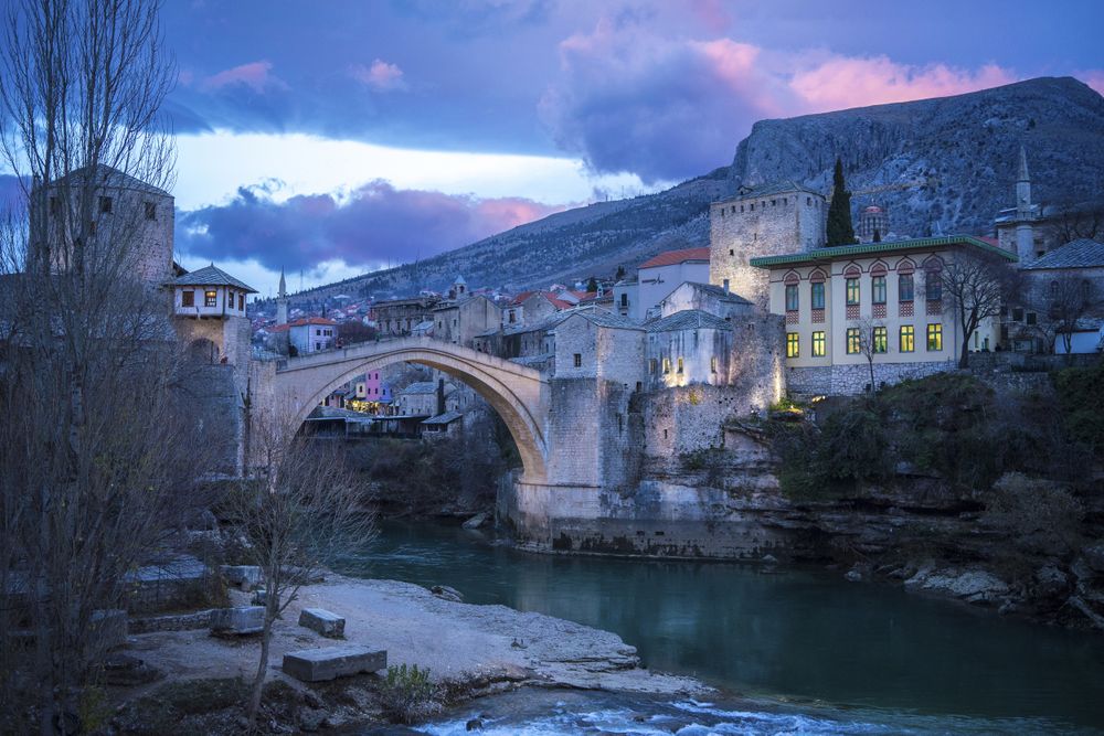 Amazing landscape of medieval bridge and aged buildings under vibrant dramatic clouds during sunset