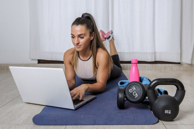 Woman laying forward on yoga mat using laptop