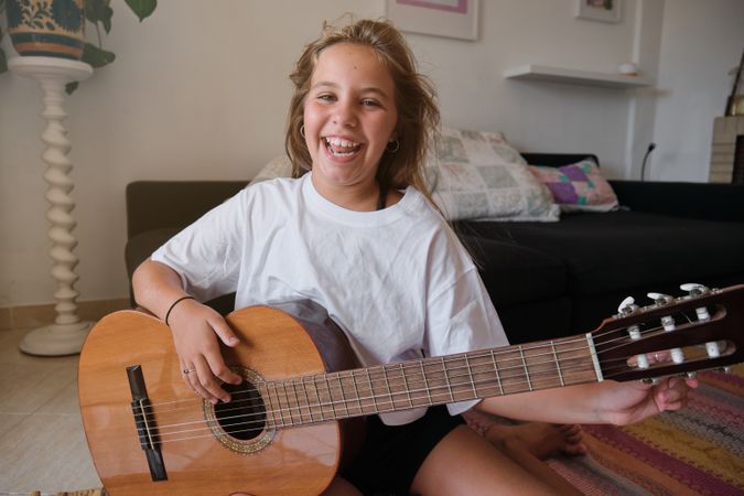 Smiling girl looking at camera while tuning a guitar in a house