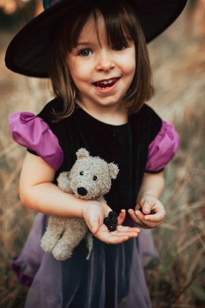 Happy girl with berries, teddy bear and witch costume