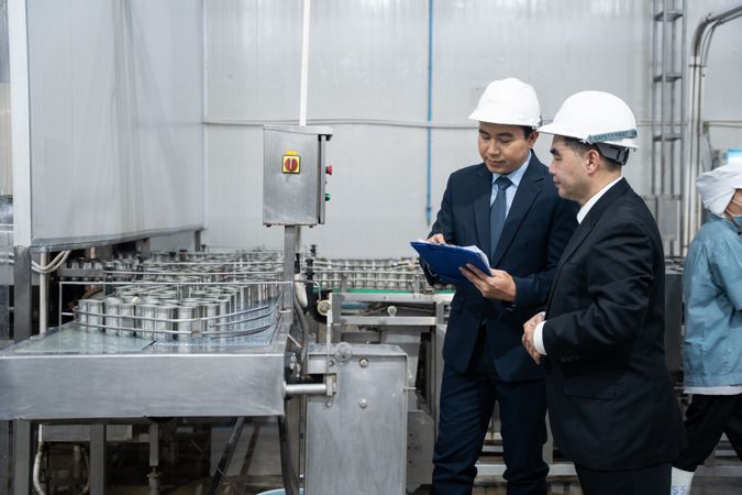 A businessman inspecting canned fish on conveyor belt at the factory