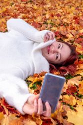 Woman lying in autumn leaves taking selfie