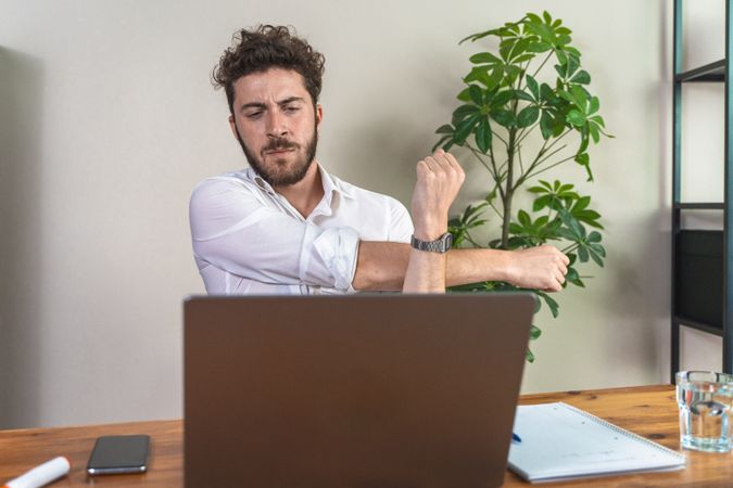 Young man stretching at his office desk during a work break.