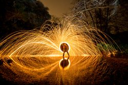 Person with burning circle on stones between water near hills at night