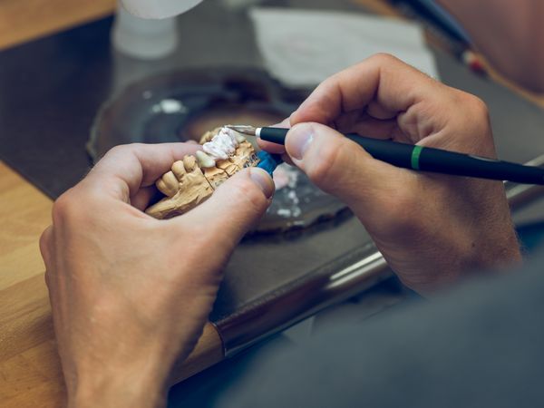 Anonymous dental technician with professional brush applying pai