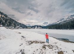 Unrecognizable person standing in snow surrounded by forest and mountains