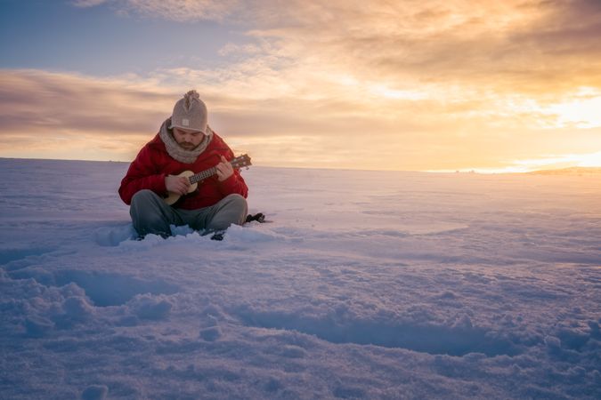 Person sitting on snow against sunset sky playing guitar