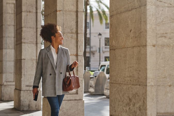 Glad Black woman with bag and phone walking on street