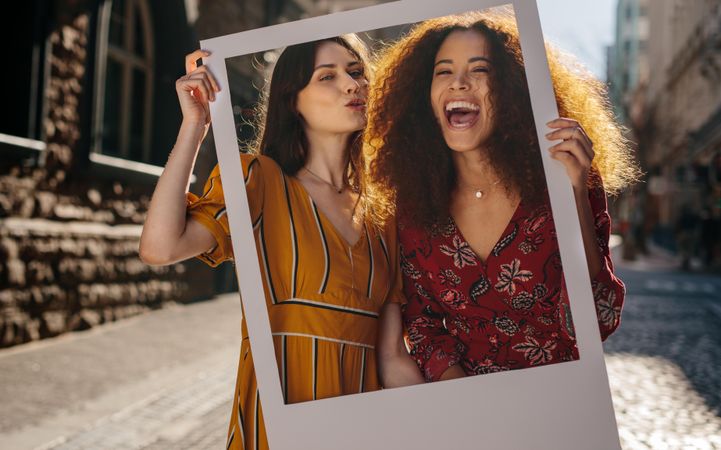 Excited young women holding an empty picture frame while standing outdoors