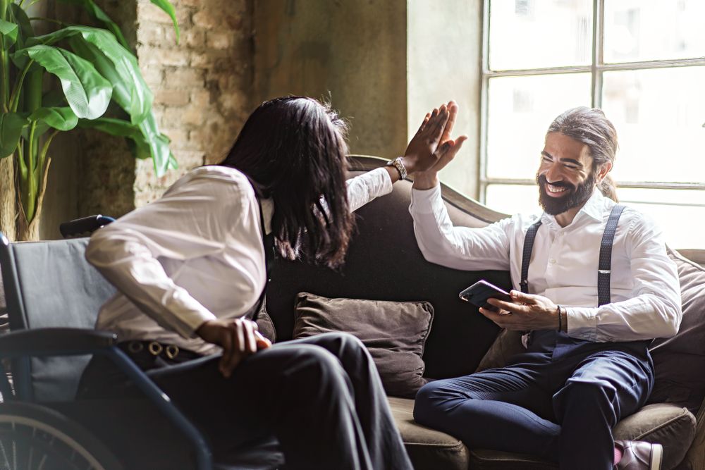 Businesswoman in wheelchair high fiving with colleague in the office