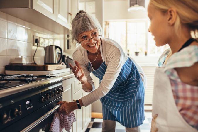 Smiling older woman in apron opening the oven door