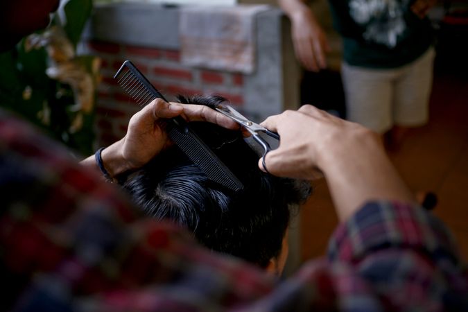 Hands of a barber cutting male client’s hair with scissors