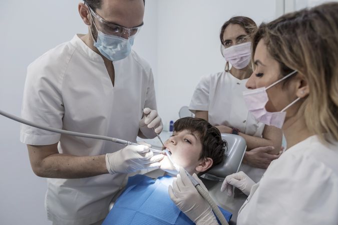 A portrait of a dentist with his team working on teenager patient
