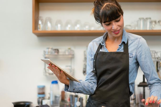 Female coffee shop owner wearing apron using digital tablet