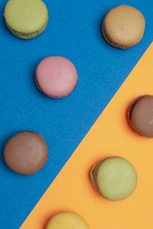 Top view of French pastel macaroons scattered on a blue and orange table