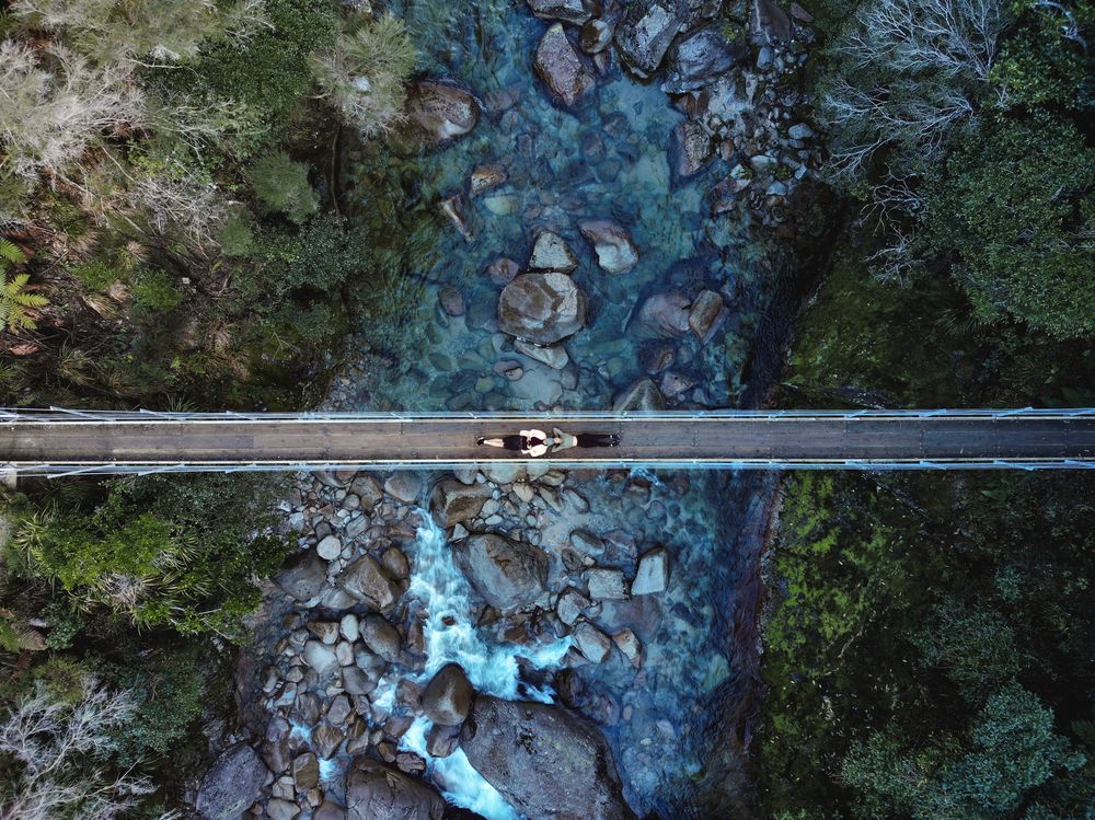 Aerial view of person riding a bike in a narrow bridge over river