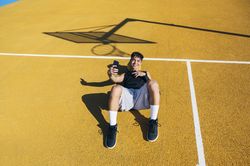 Male basketball player using his smartphone resting after training