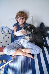 Smiling preteen schoolboy in glasses sitting on bed with dog