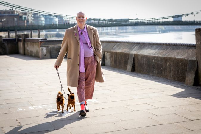 Mature man walking by river with two small dogs