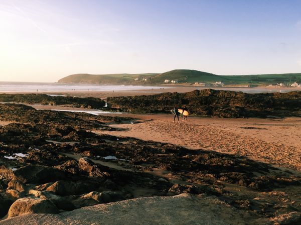 Surfers walking towards water at rugged coast line at dawn