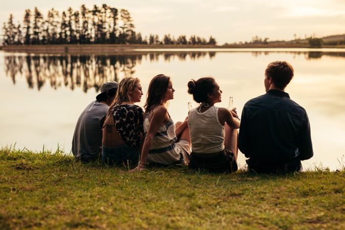 Rear view portrait of group of young friends relaxing by a lake