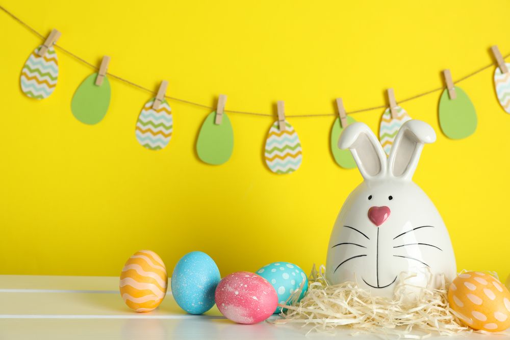 Decorated bunny and Easter eggs on table against color background