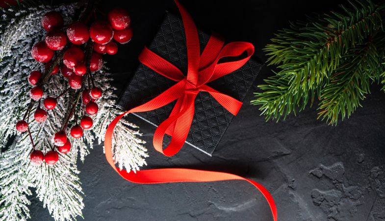 Top view of Christmas gift with holly and branches on concrete background