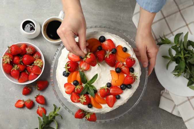 Woman puts mint on berry cream cake. Delicious dessert