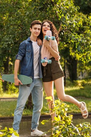 Happy teenage couple standing with skateboards in city park