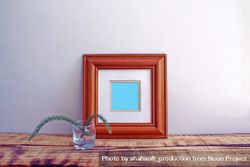 Square wooden picture frame on wooden desk with branch mockup 43LXxb