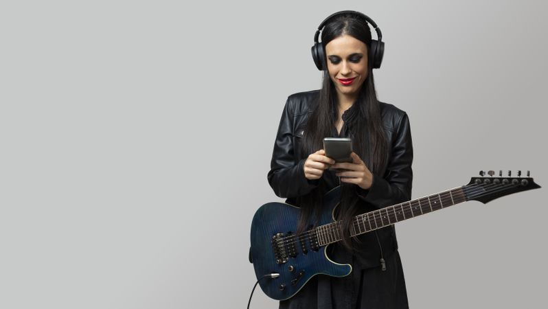 A female guitarist, enjoys listening to music with headphones from the mobile phone she holds in her hands
