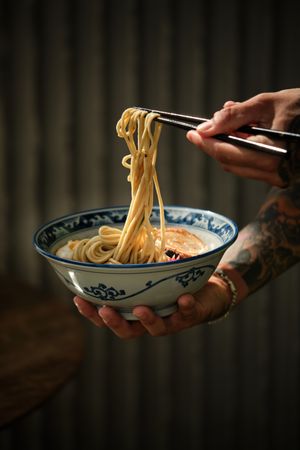 Crop person having noodles in bowl with chopsticks
