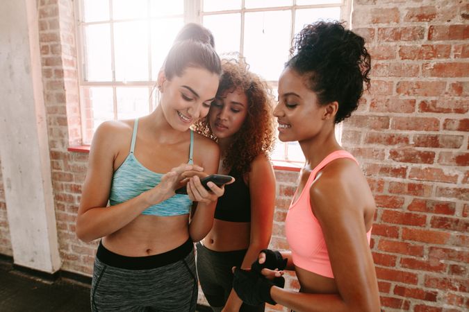Group of young females looking at smartphone and smiling after exercise