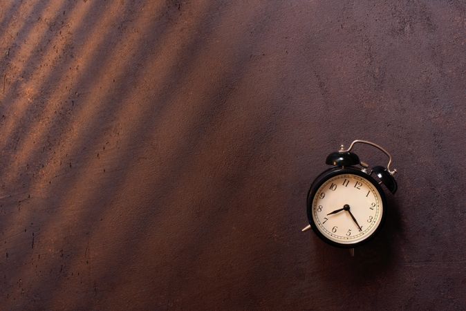 Traditional alarm clock with shadows on brown background