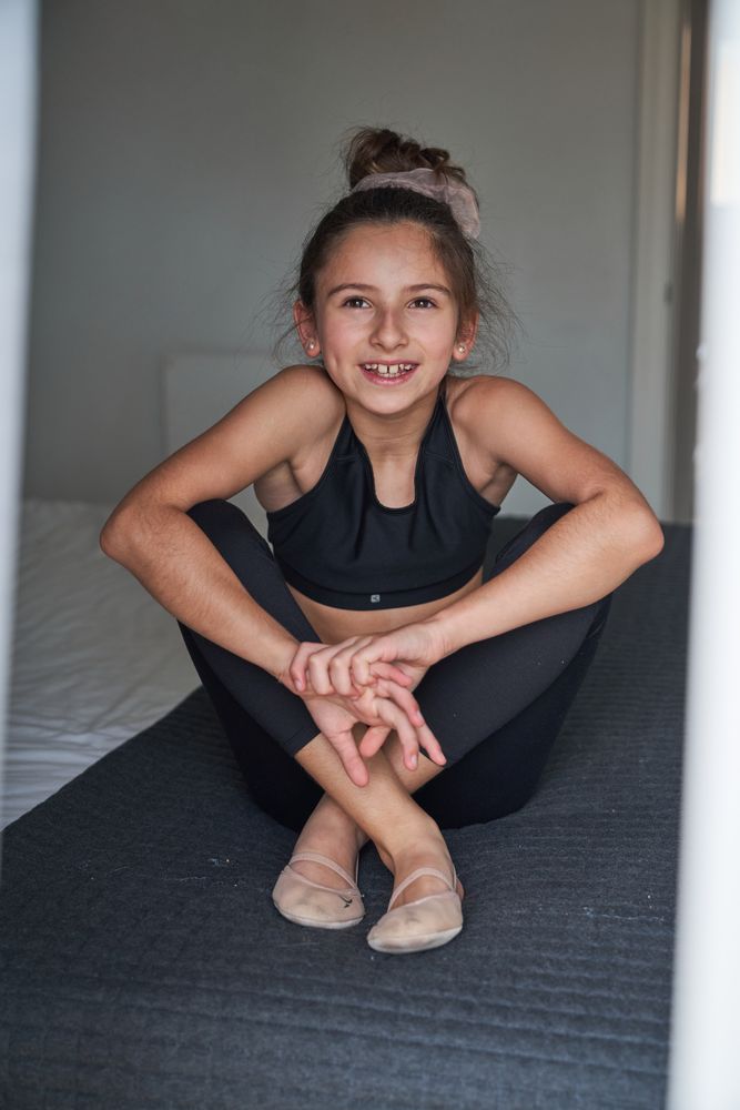 Smiling preteen gymnast in sportswear sitting on bed