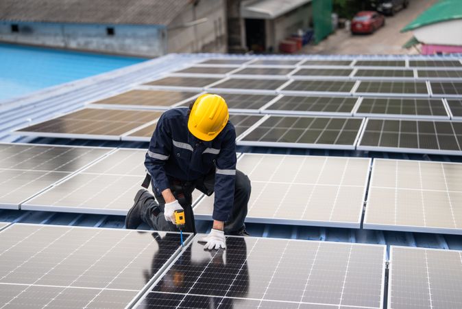 Engineer worker using electric drill repairing on solar cell panel on the roof of the factory. After service and security for industrial renewable energy concept